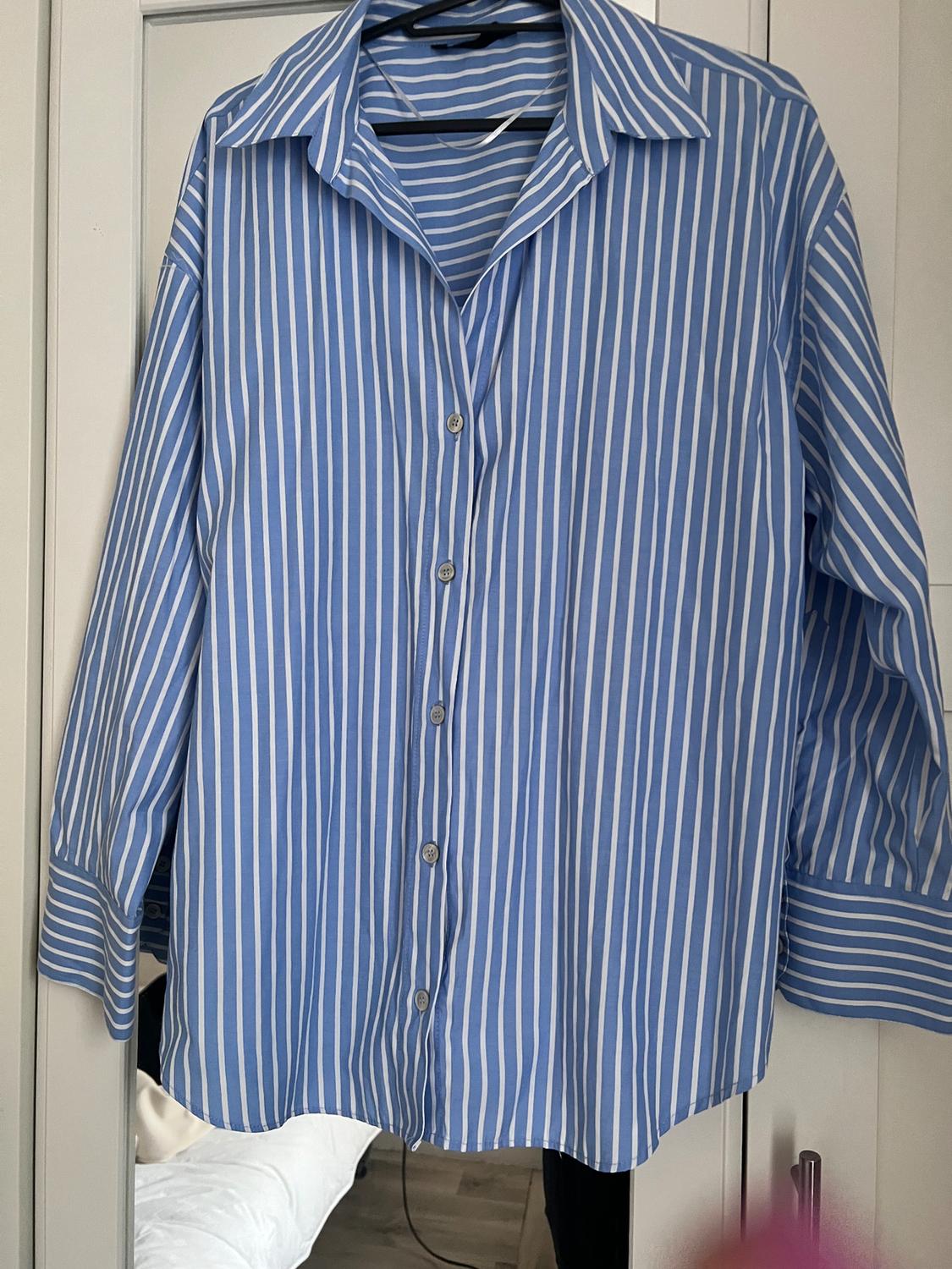 Blue and white striped shirt hanging on a hanger in front of a white wardrobe. Background with partially visible bed.