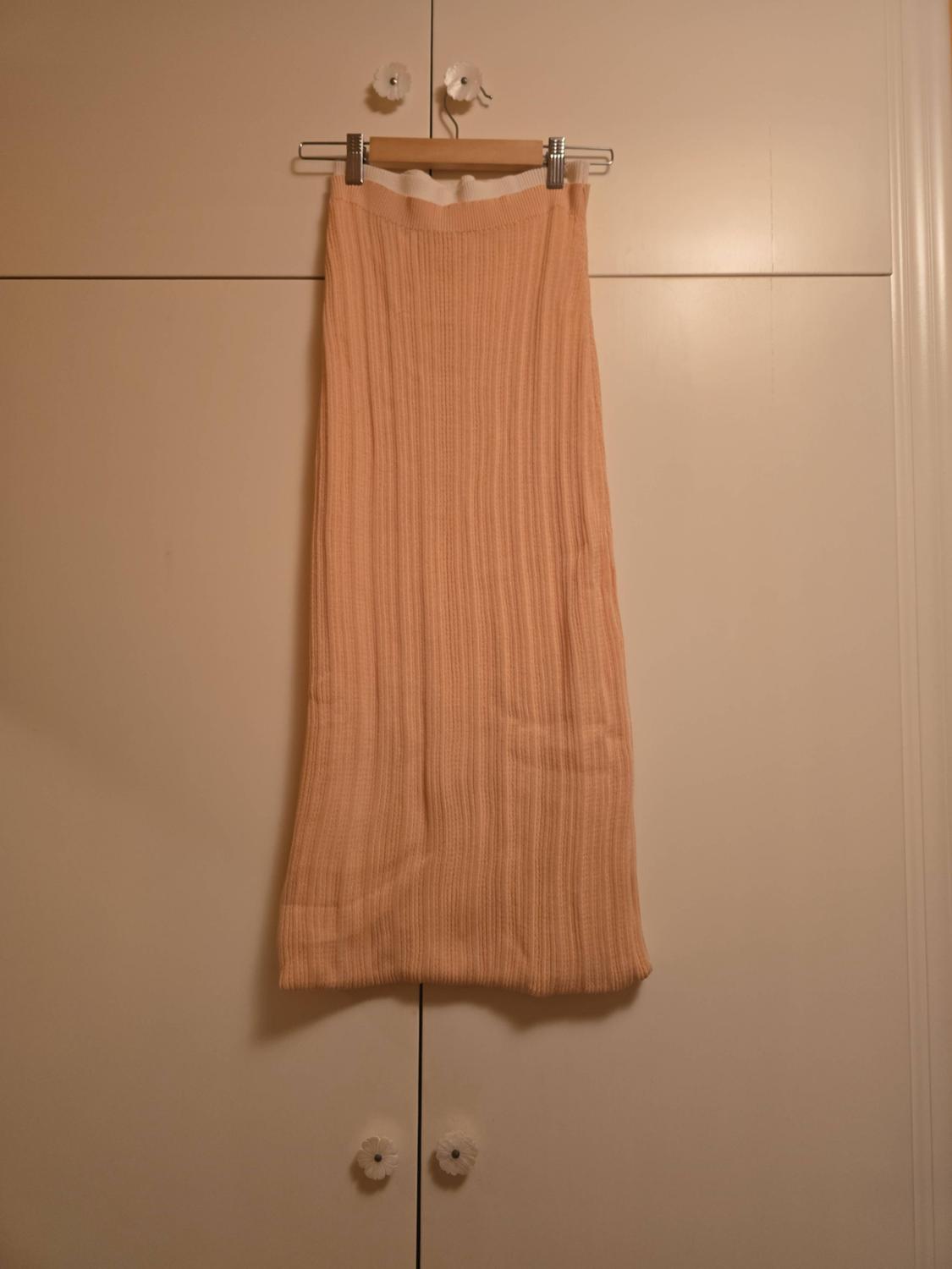 Light peach ribbed knitted skirt hanging on a wooden hanger inside the doors of a white wardrobe.