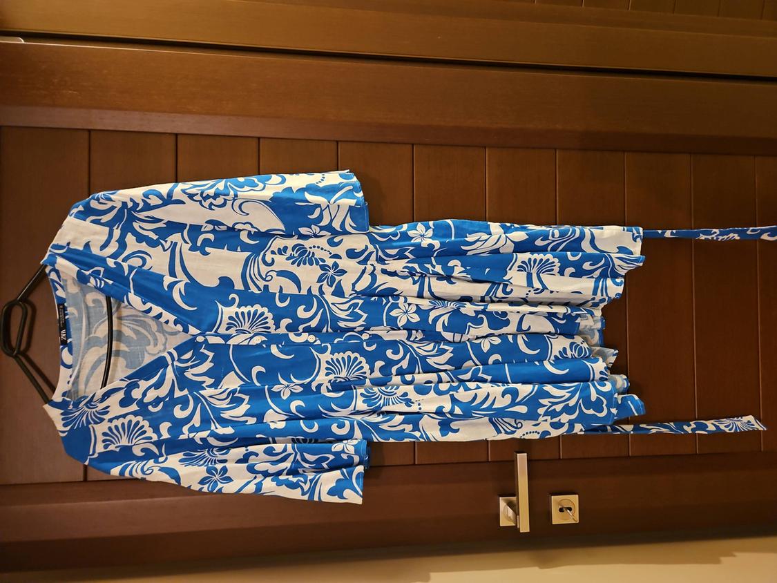 Dress hanging on a wooden door, with a blue and white floral print, and a matching belt.