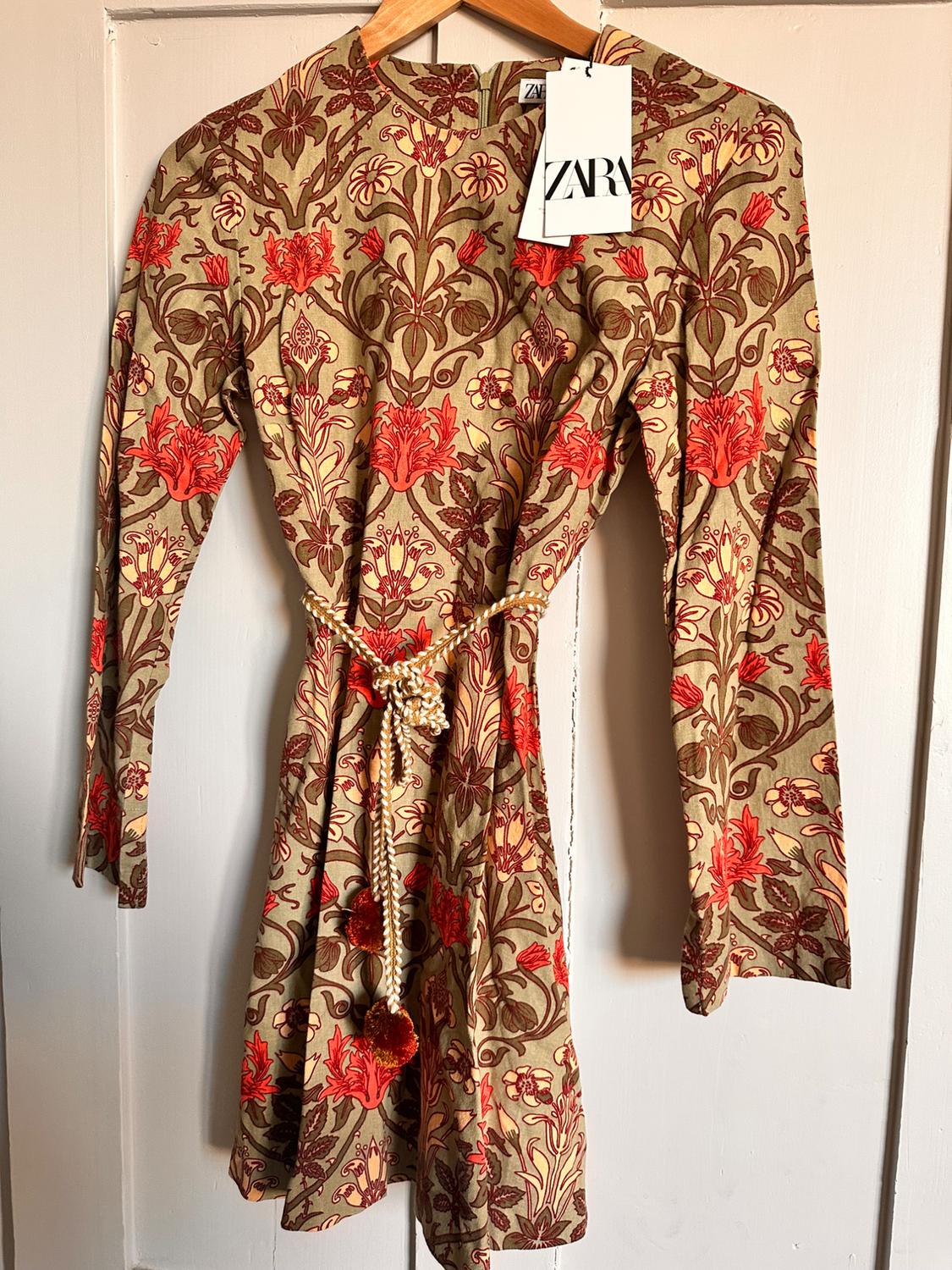 Long-sleeved dress with a floral print in shades of brown and red, hanging on a hanger. Visible label with the text "ZARA".