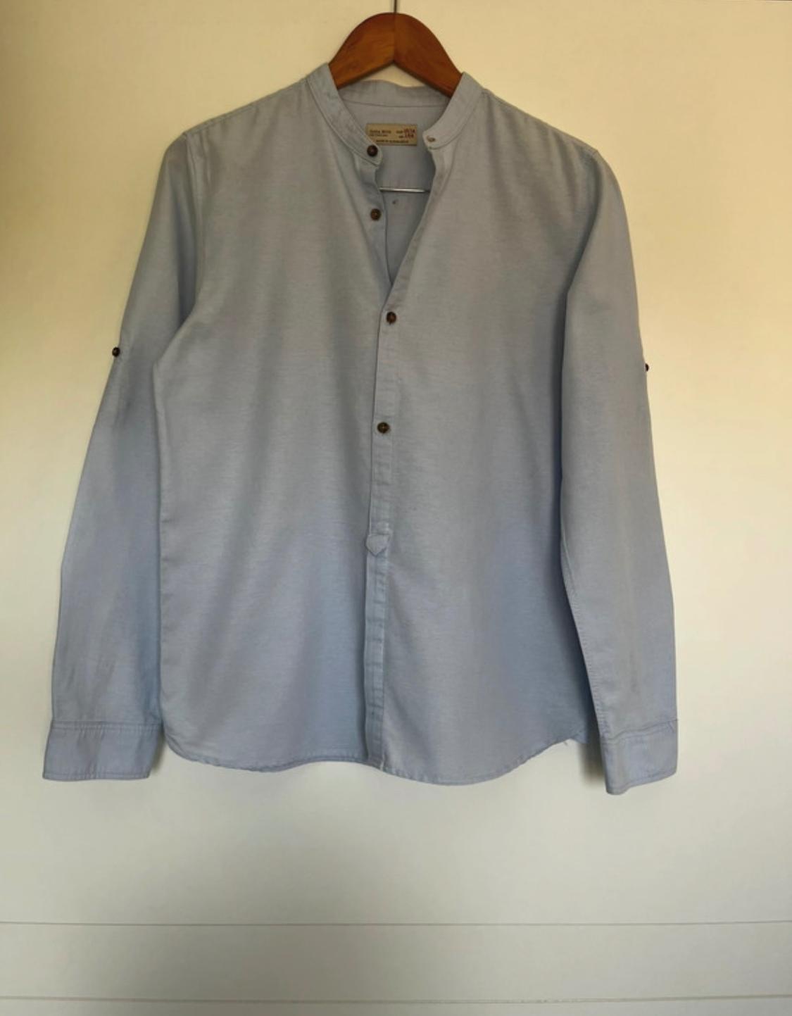 Front view of a light blue shirt with a mandarin collar and dark buttons.