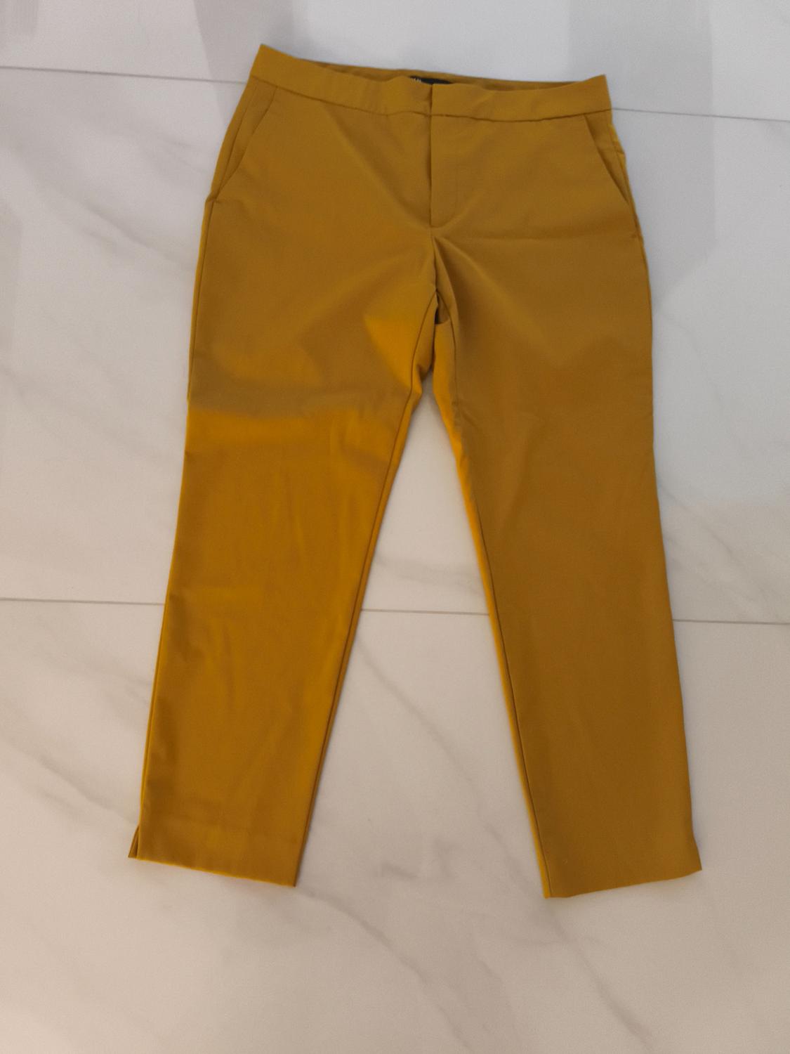 Mustard straight-leg trousers with pockets and openings at the hem, laid out on a white marble tiled floor.