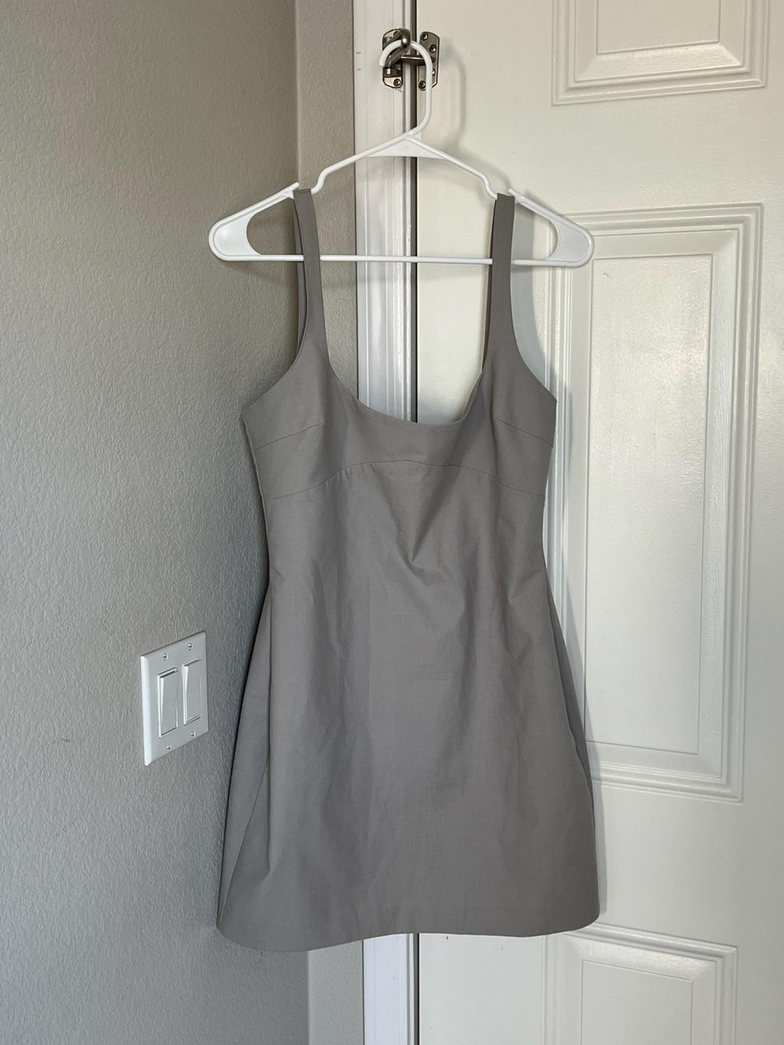 Short grey dress with wide straps hanging on a white door. Relaxed and casual home setting with a grey wall.