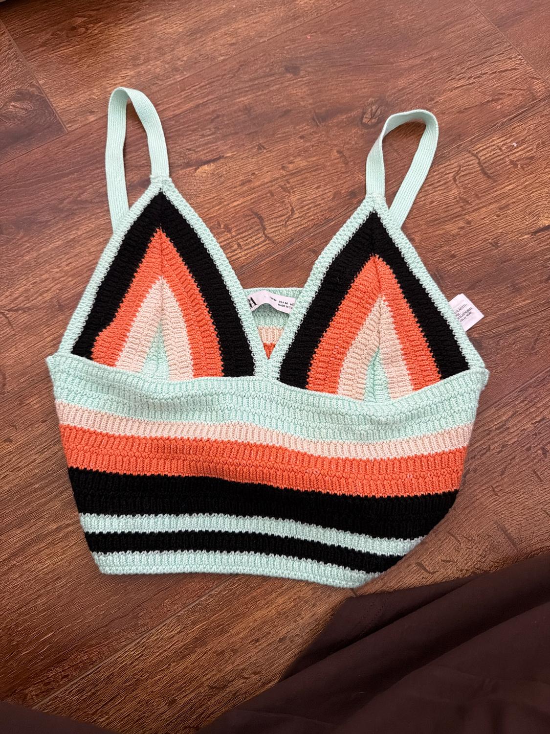 Crochet top with thin straps in black, coral and mint tones, on a brown wooden background.