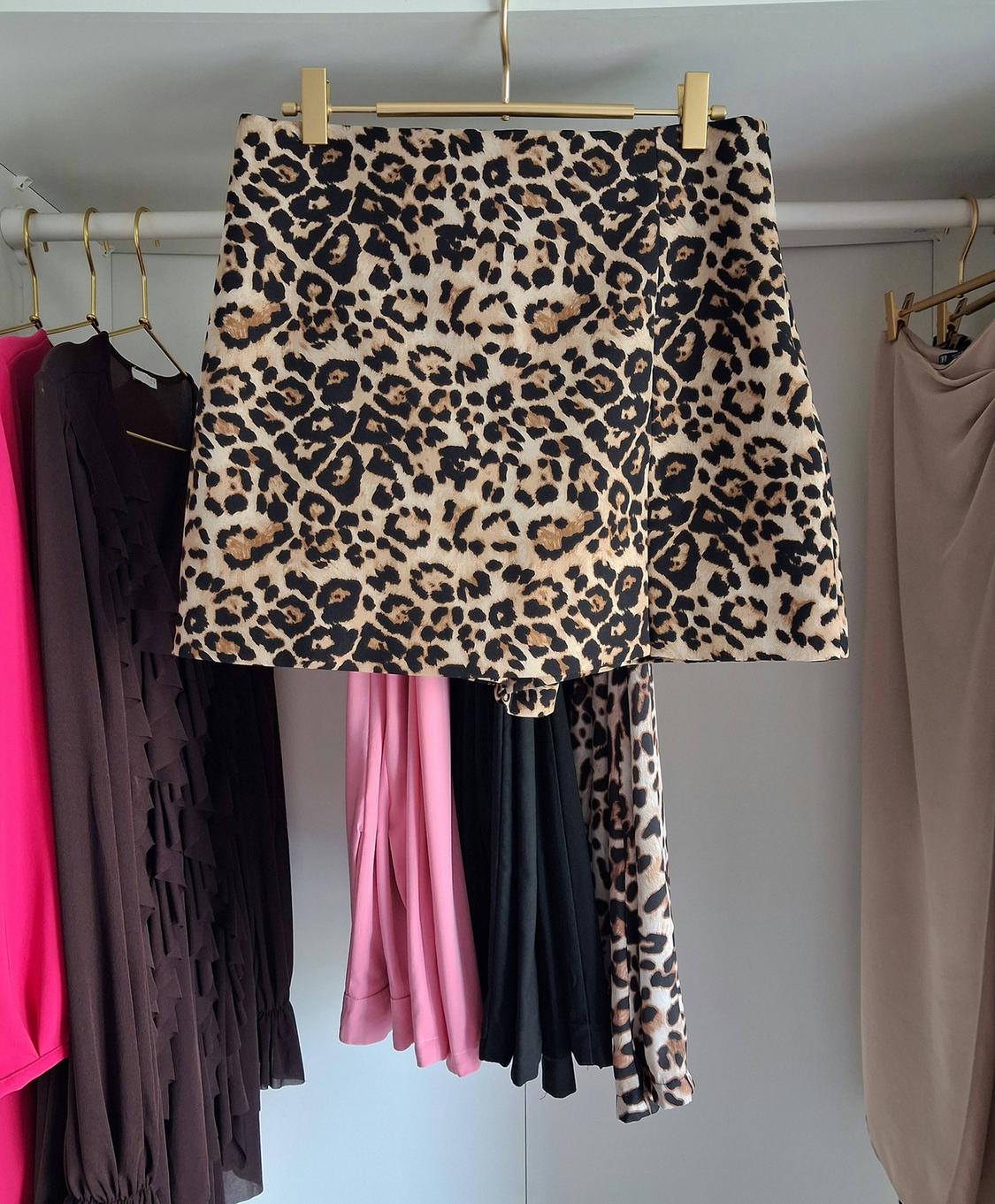Leopard print skirt hanging in a wardrobe next to other pink, black, and brown garments.
