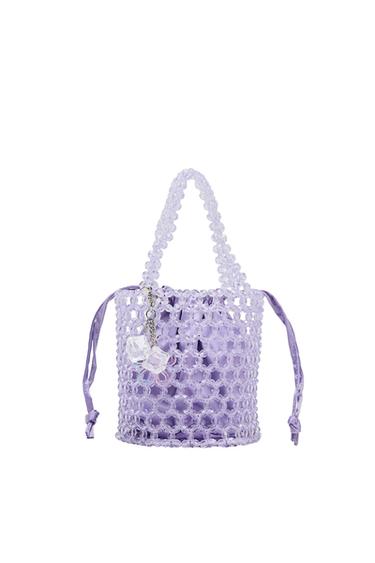 Lilac beaded handbag on a white background. It has short handles, a satin fabric interior with drawstring closure, and a decorative transparent charm.