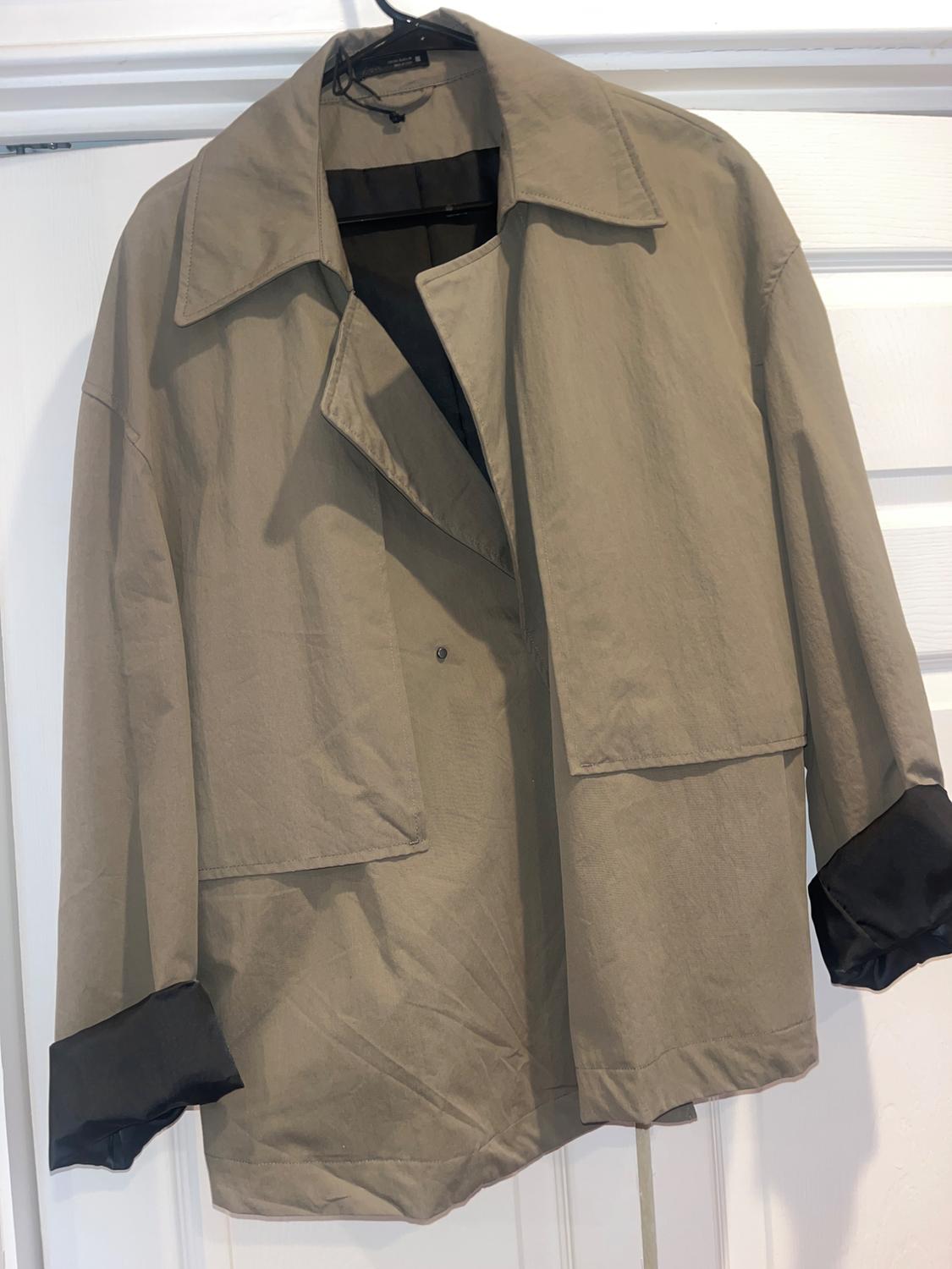 Beige jacket hanging on a black hanger, with wide lapels and dark cuffs, on a white door.