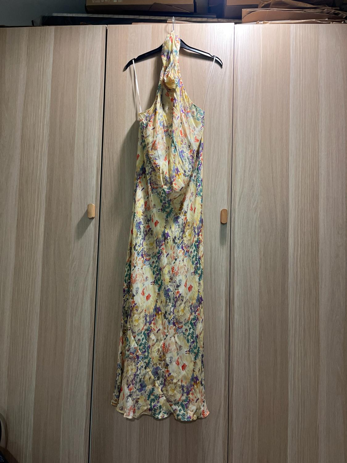 Long halter-neck dress with a multicoloured floral print, hung on a black hanger in front of a light oak wardrobe.