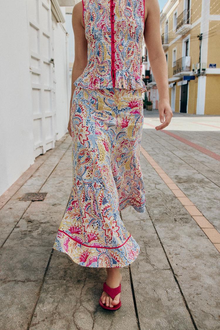 Button-up sleeveless top and A-line midi skirt set, both featuring a multicoloured print with contrasting pink piping. Pink sandals.