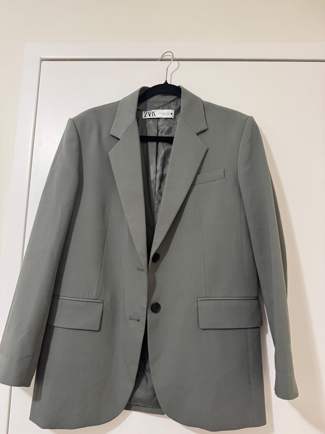 Gray suit jacket hanging on a black hanger over a white door. Visible tag with the text "ZARA".