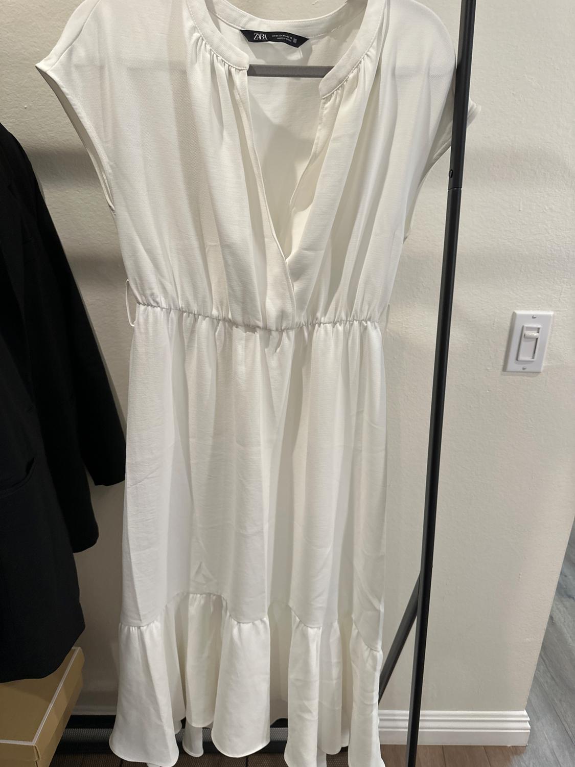 Front view of a white dress with a V-neck and short sleeves, an elasticated waist and a ruffled skirt.