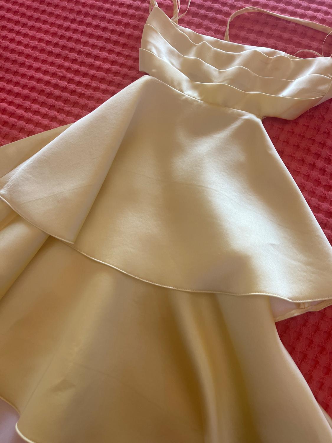 Light yellow satin dress with spaghetti straps, a pleated bodice, and a tiered skirt, over a textured pink fabric.