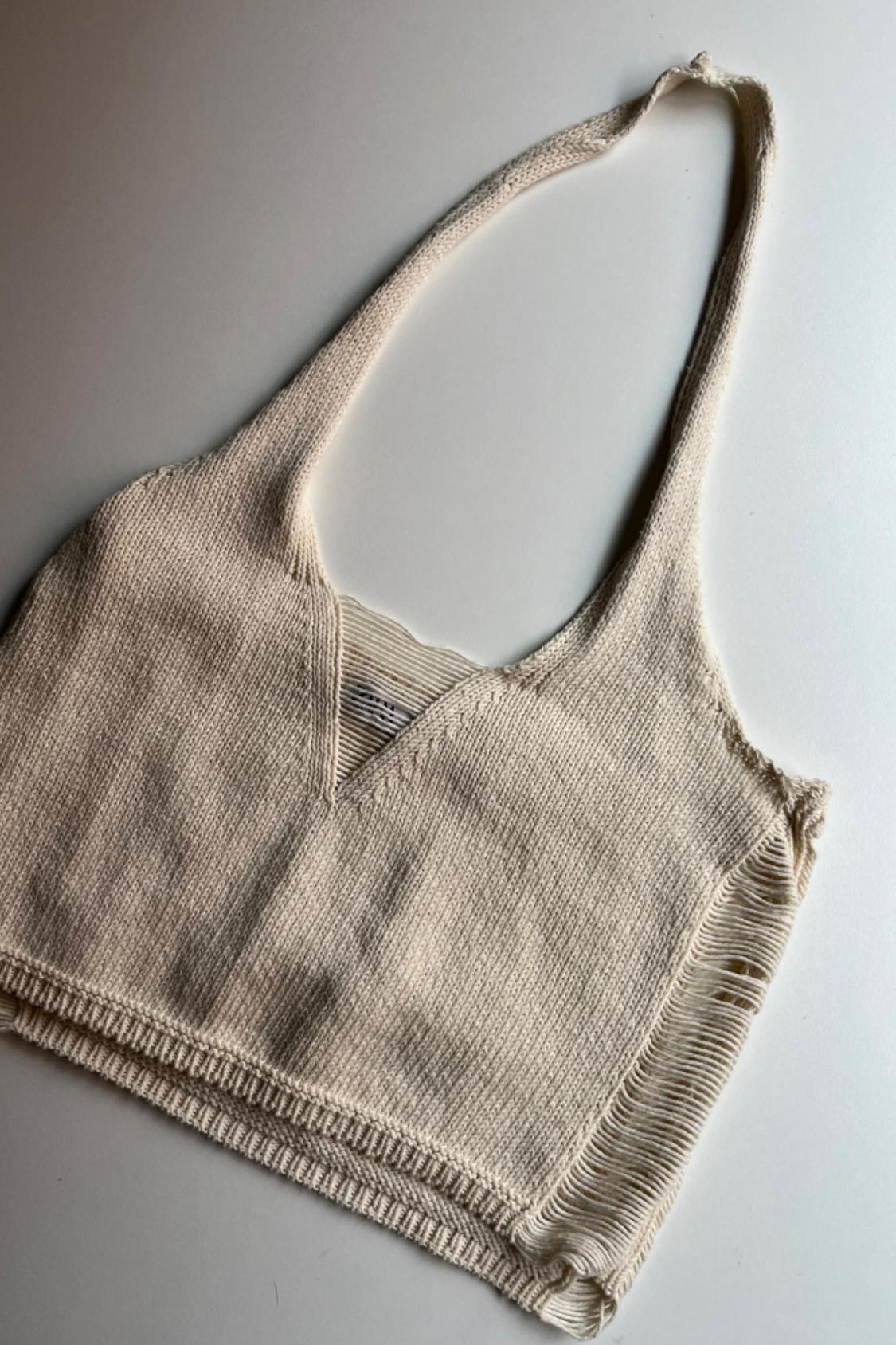Front view of a beige knitted top with a V-neck and ribbed detailing on the edges.
