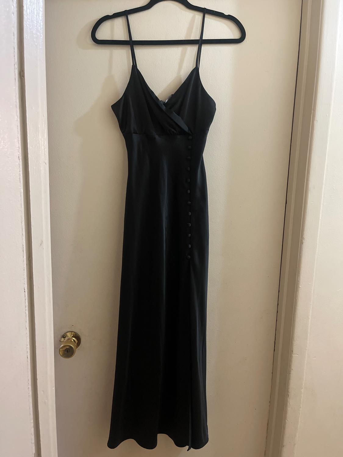 Long black dress with thin straps and buttons down the front, hanging on a black hanger over a white door.