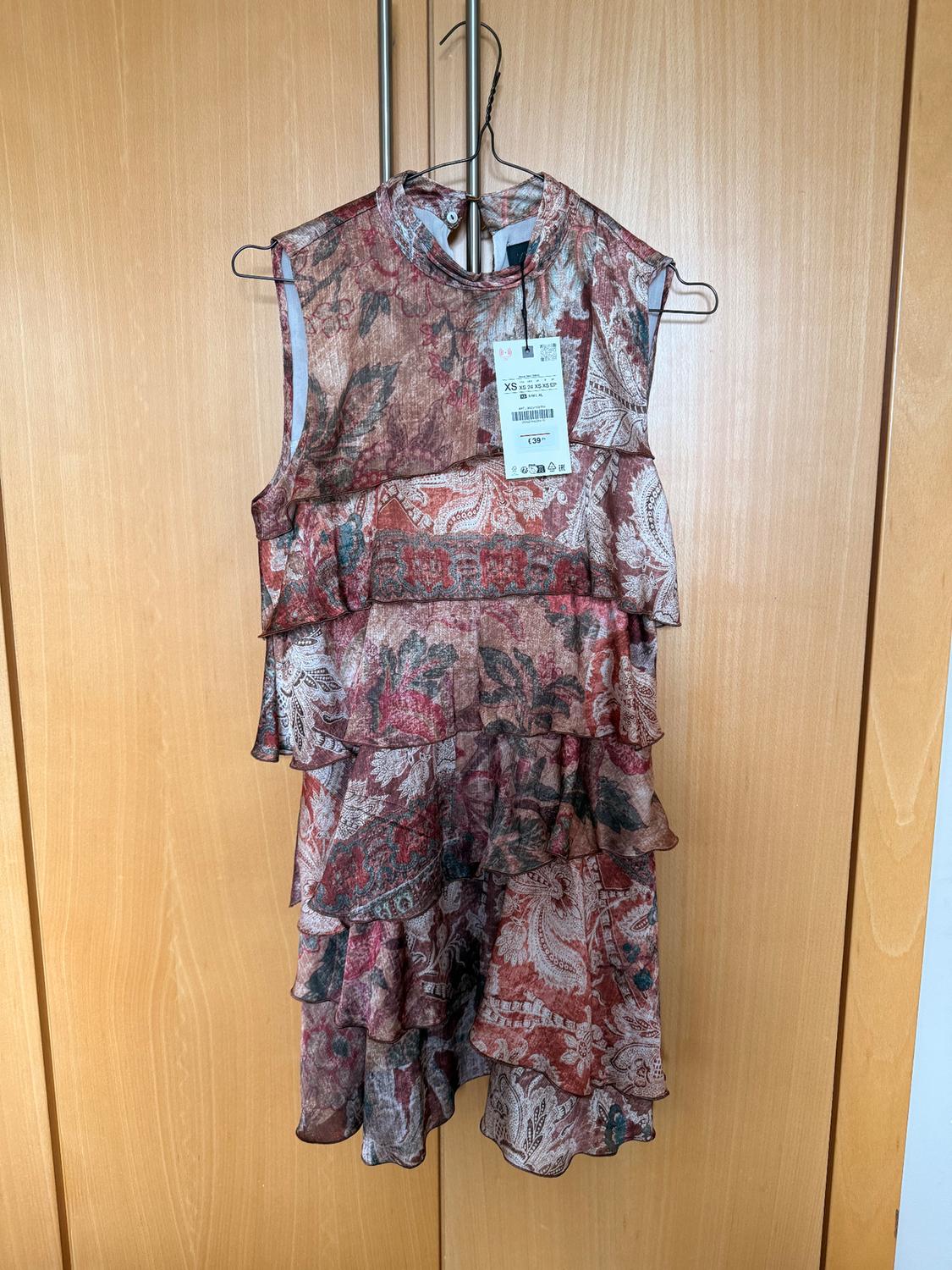Sleeveless floral print dress with ruffles, hanging on a metal hanger. Visible label with size XS and price £39.99.