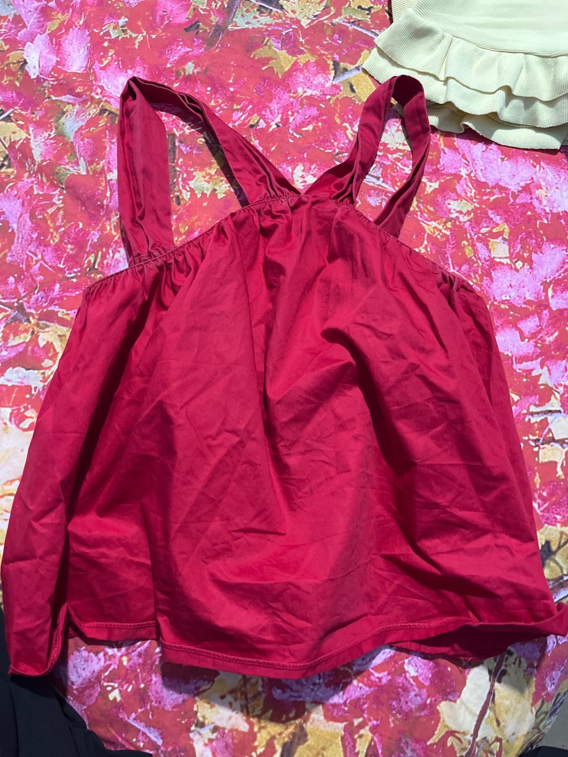 Red strappy top on a pink and yellow floral background, next to a beige ruffled garment.