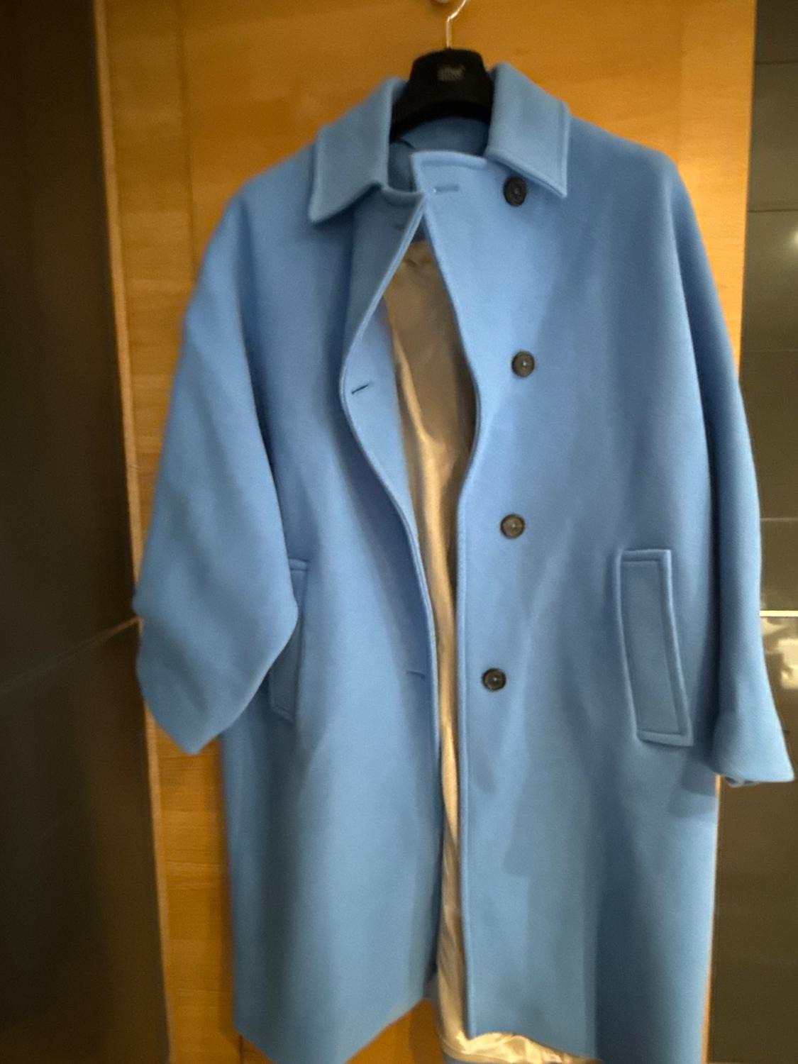 Light blue coat hanging on a black hanger against a wooden background. The coat has dark buttons and a visible inner lining.