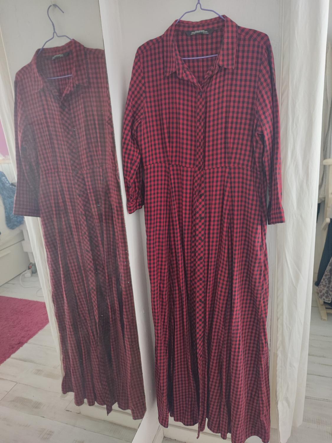 Red and black checked maxi dress hanging on a hanger, reflected in a mirror in a bright room.