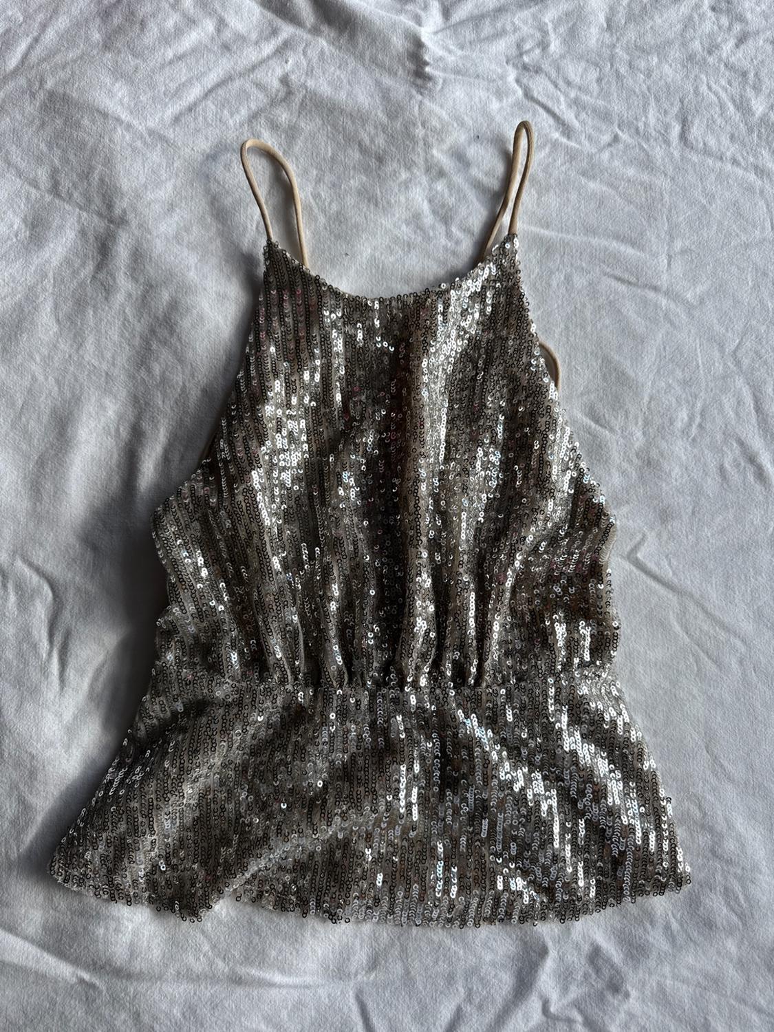 Silver sequin top with thin straps and a ruched waist, on crumpled white fabric.