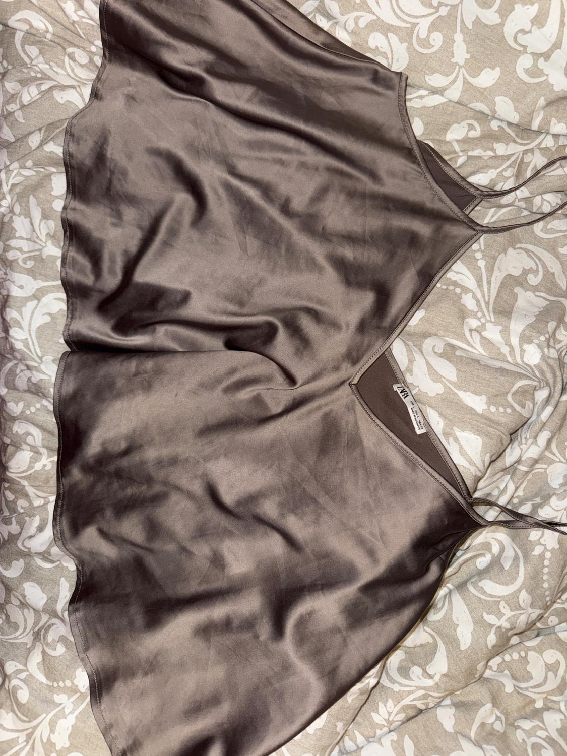 Satin brown camisole top on a floral patterned bedspread in beige and white tones. Visible label with text "ZARA".