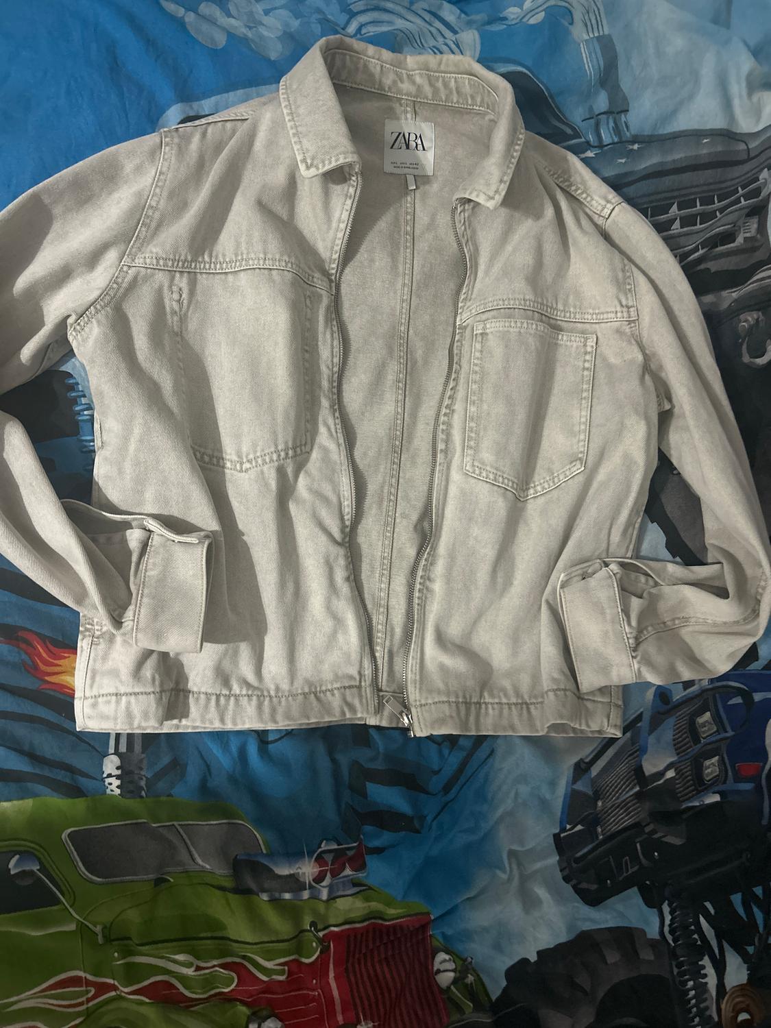 Light grey zip-up jacket with front pockets on a blue car-patterned duvet. Visible label: ZARA.