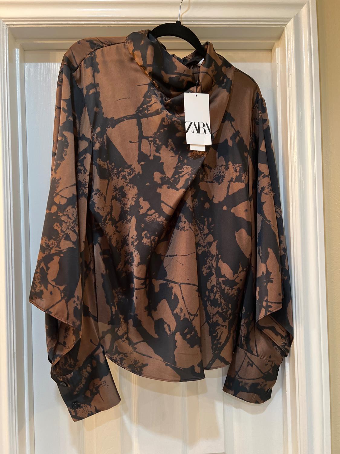 Brown and black blouse with abstract print, hanging on a white door. Visible label with the text "ZARA".