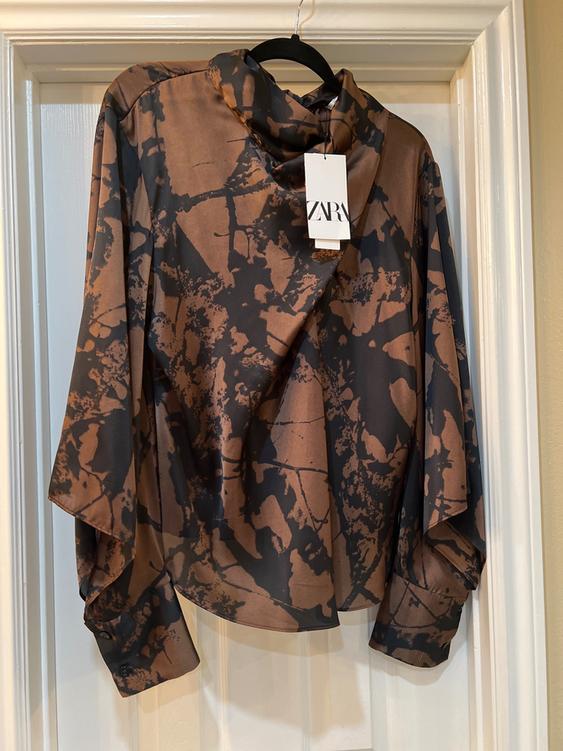 Brown and black blouse with abstract print hanging on a white door. Visible tag with the text "ZARA".