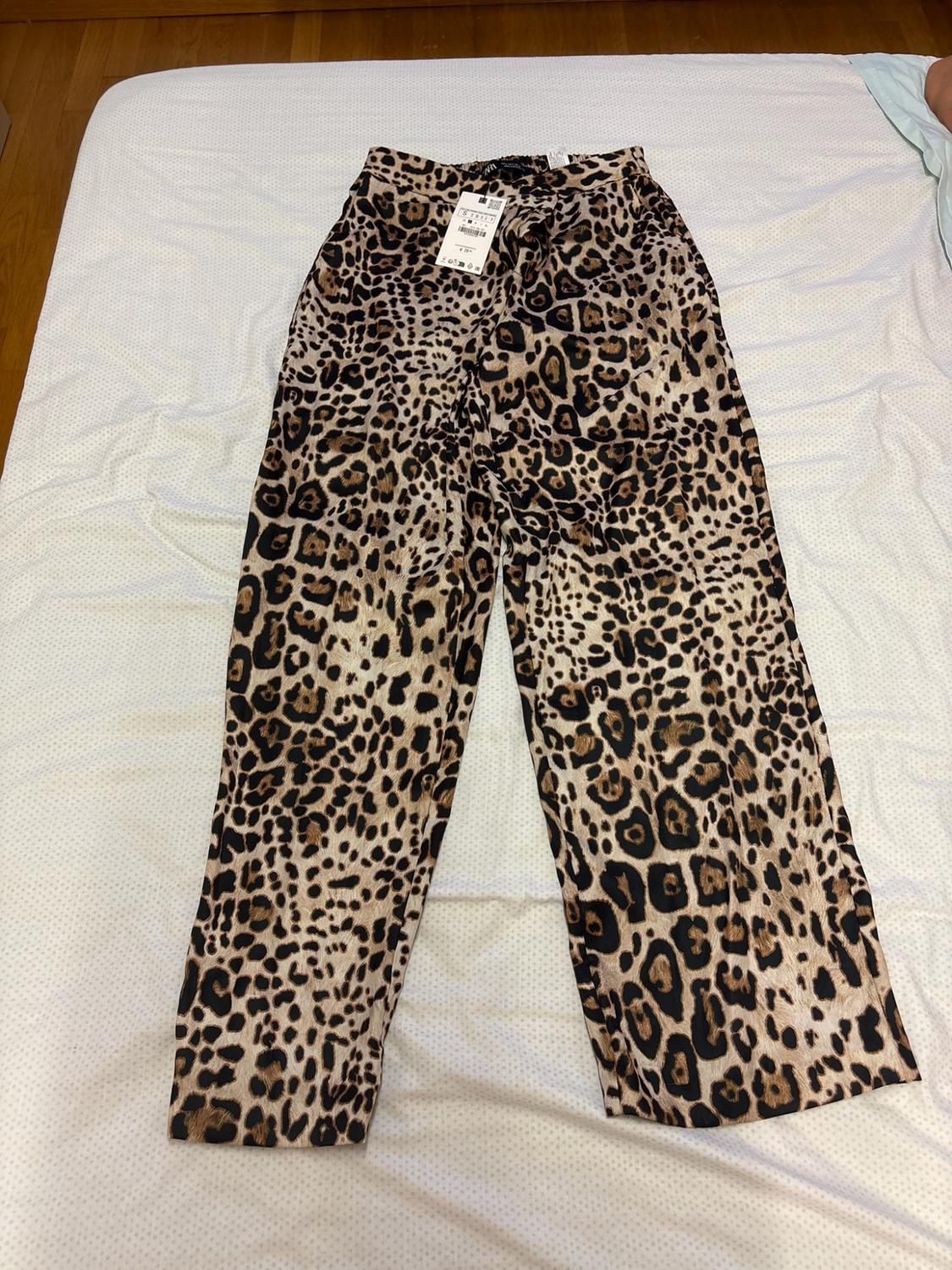 Trousers with a leopard print and a label at the waist, laid out on a white sheet.