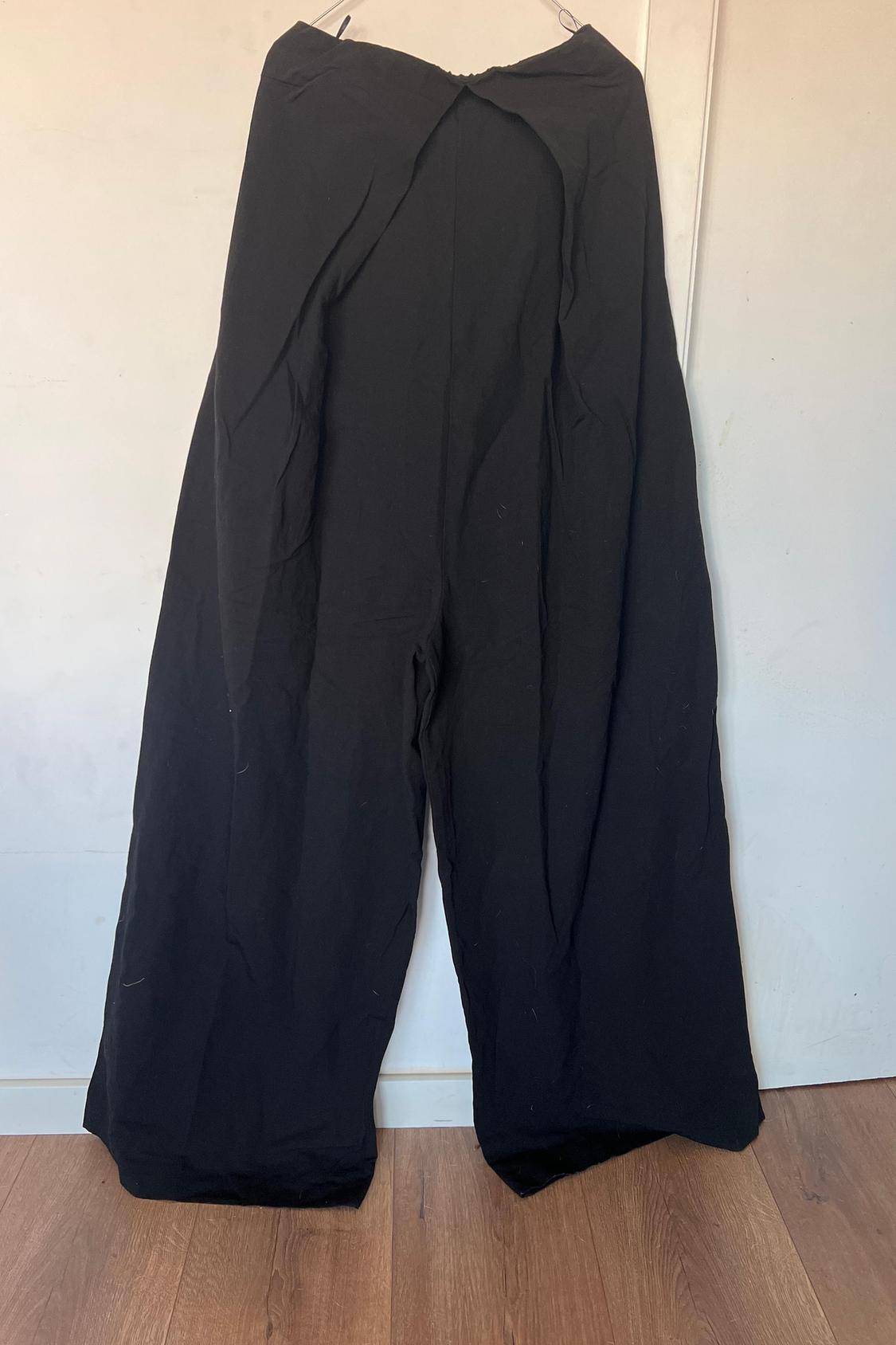 Front view of wide black trousers hanging on a hanger.