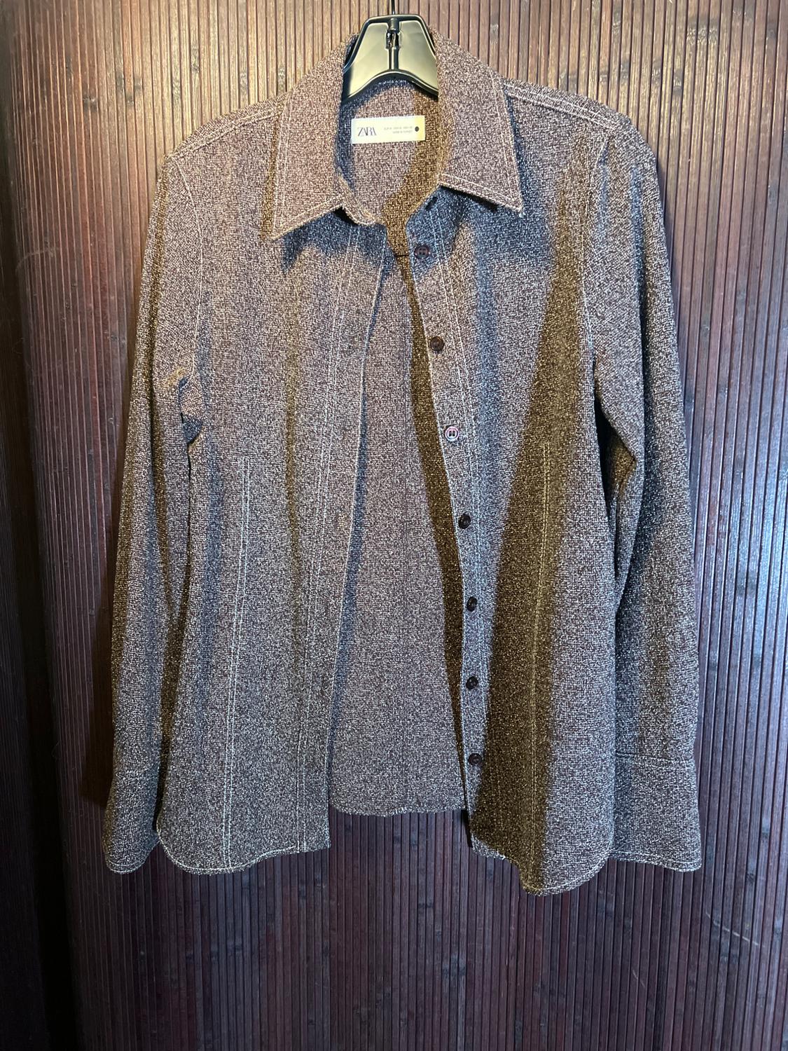 Textured gray shirt hanging on a black hanger against a dark wood background. Visible label with the text "ZARA".