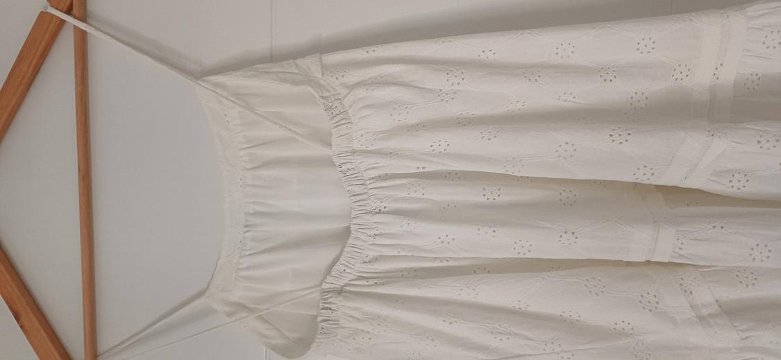 White, thin-strapped dress with floral embroidery, hanging on a wooden hanger against a white background.
