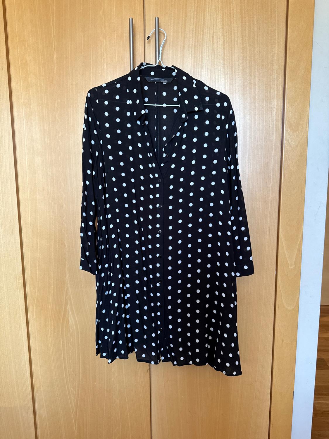 Front view of a black dress with white polka dots and long sleeves.