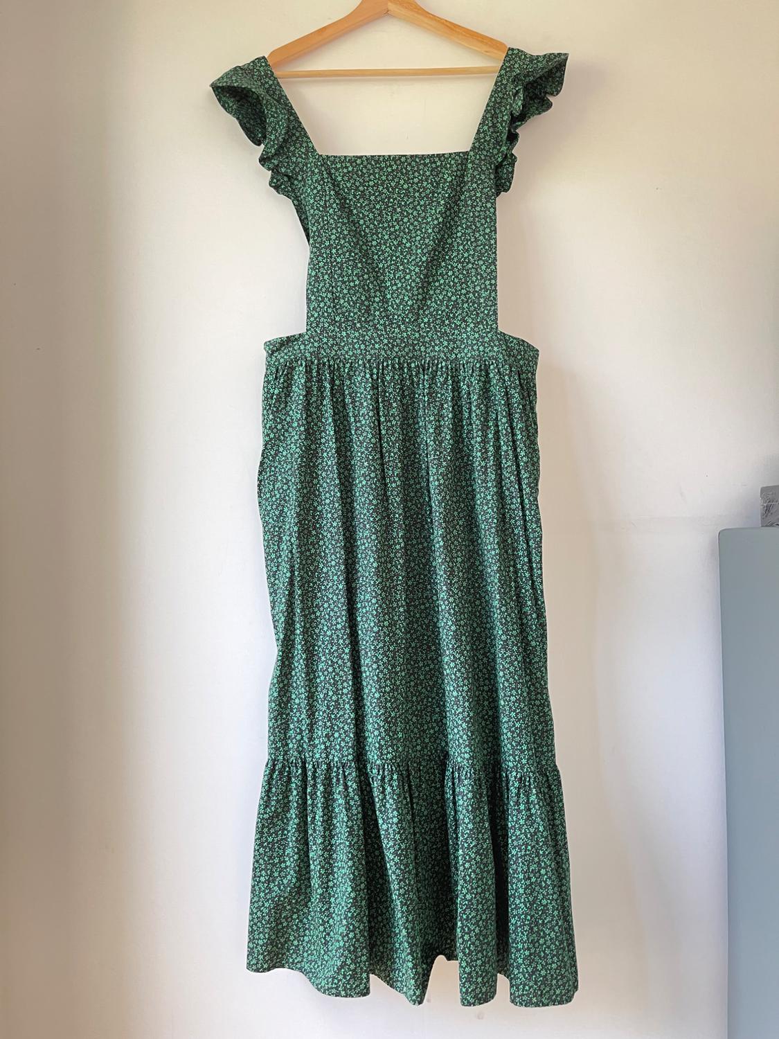 Green dress with a small floral print, wide straps and frills on the shoulders, hanging on a wooden hanger.