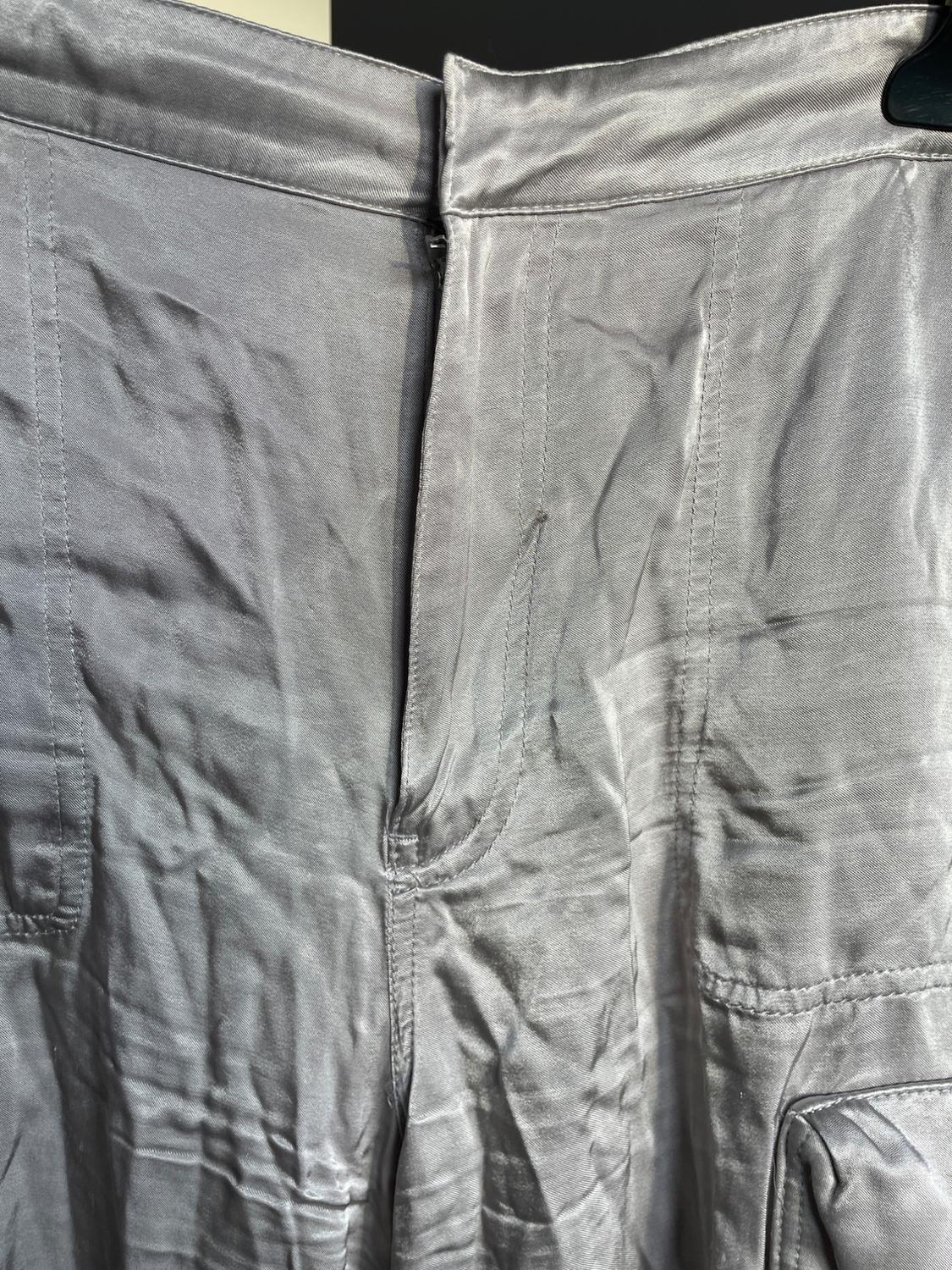Grey satin fabric trousers with a front fastening and visible seam details. The fabric has a shiny finish and creases.