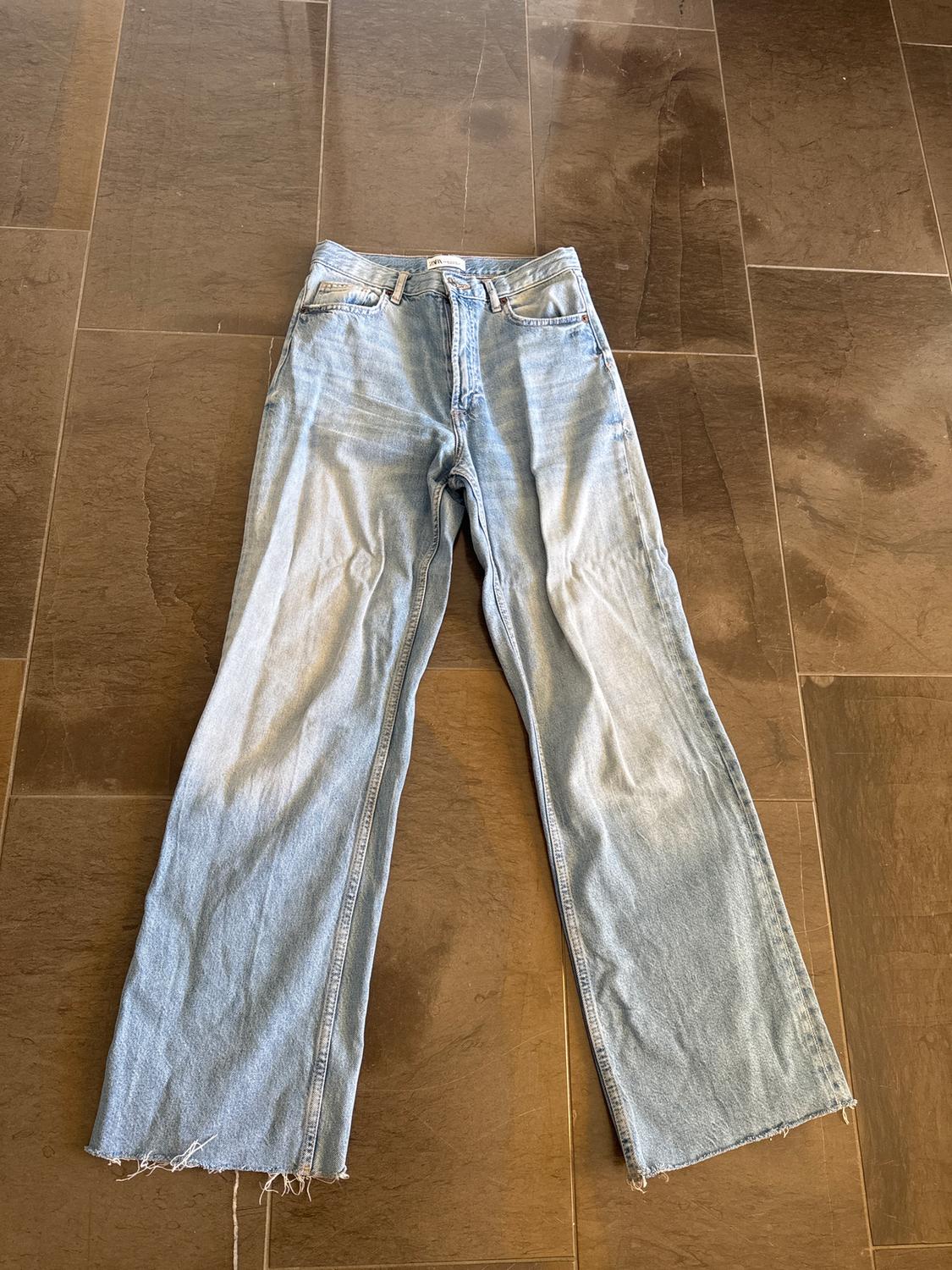 Blue wide-leg jeans with a frayed hem, placed on a brown tiled floor.