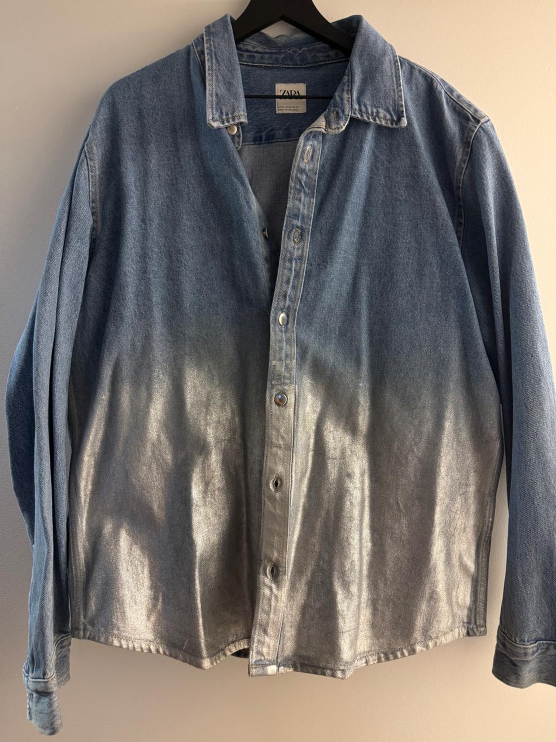Blue denim shirt with a faded silver effect, hanging on a black hanger. Visible label with text "ZARA".