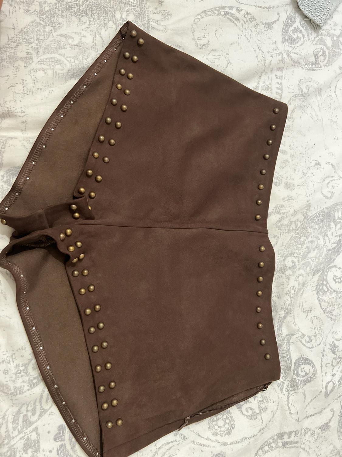 Brown shorts with decorative studs, arranged on light patterned fabric. A relaxed, casual composition.