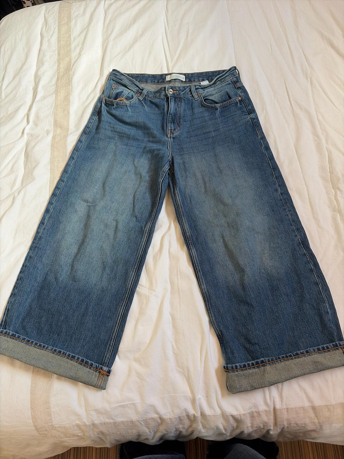 Blue wide-leg jeans with turn-up hems, laid out on a crumpled white sheet in a casual style.