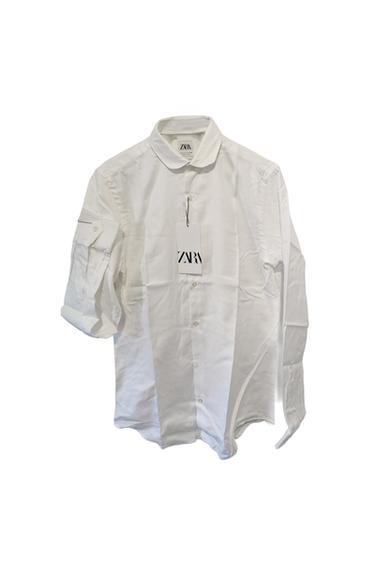 Long-sleeved white shirt with a hanging tag that reads "ZARA". One sleeve is partially rolled up. White background.