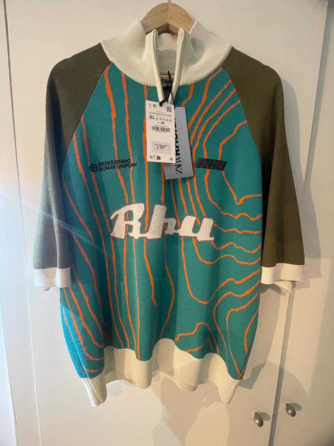 Hanging jumper with abstract design in green, orange, and white. Visible text: "Redesigning Human Uniform", "Rhu". Price tag: €59.99.