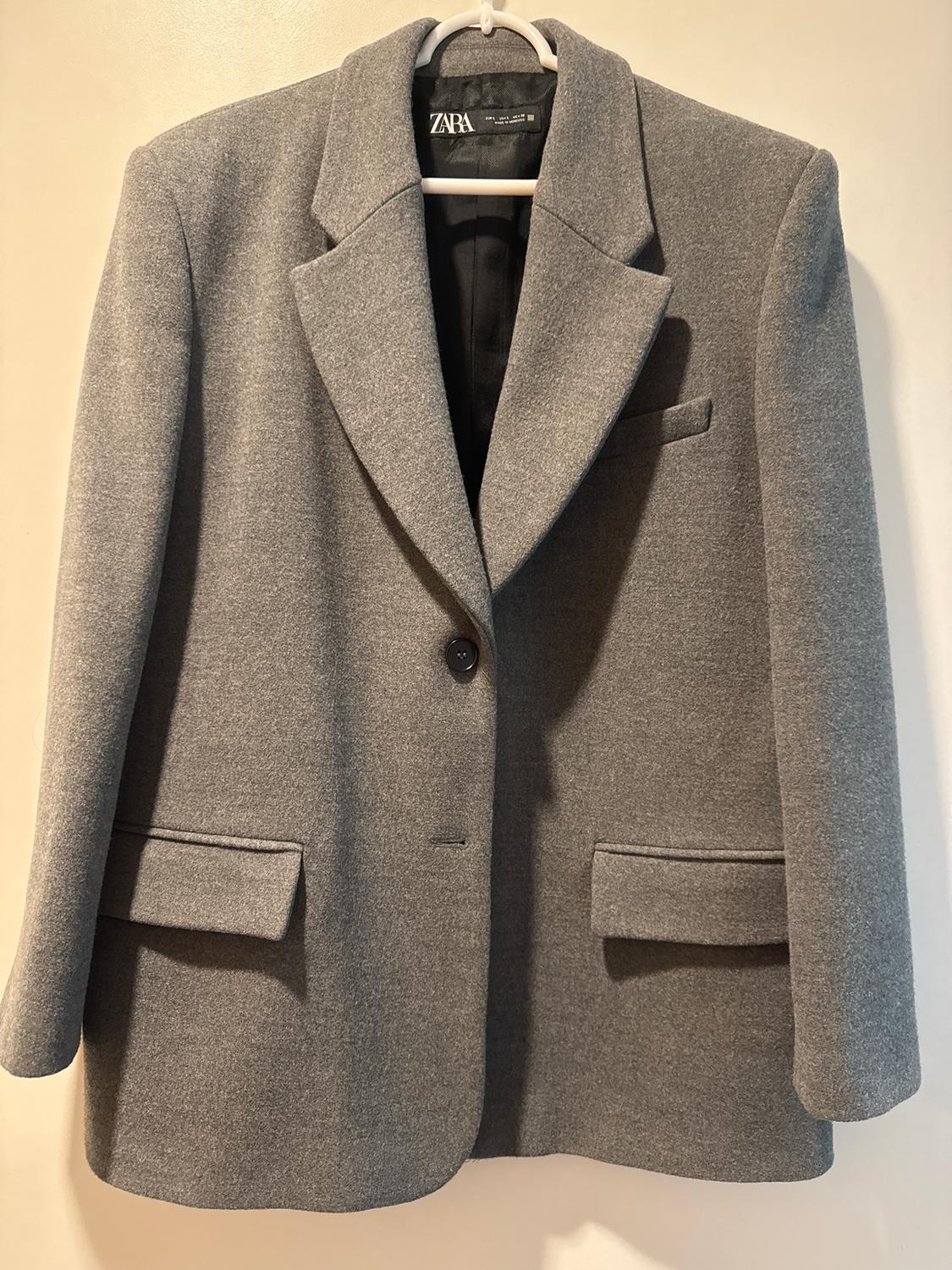 Gray wool jacket hanging on a white hanger, with wide lapels and a black button. Visible tag: ZARA.
