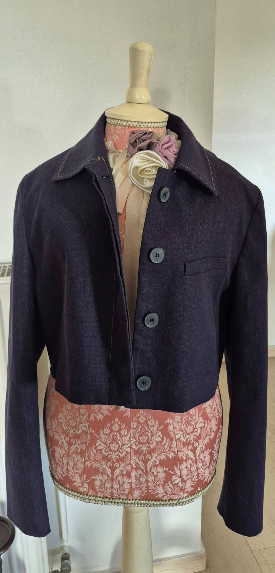 Mannequin with a dark blue short jacket with large buttons, against a white wall background. Floral decoration on the mannequin's torso.