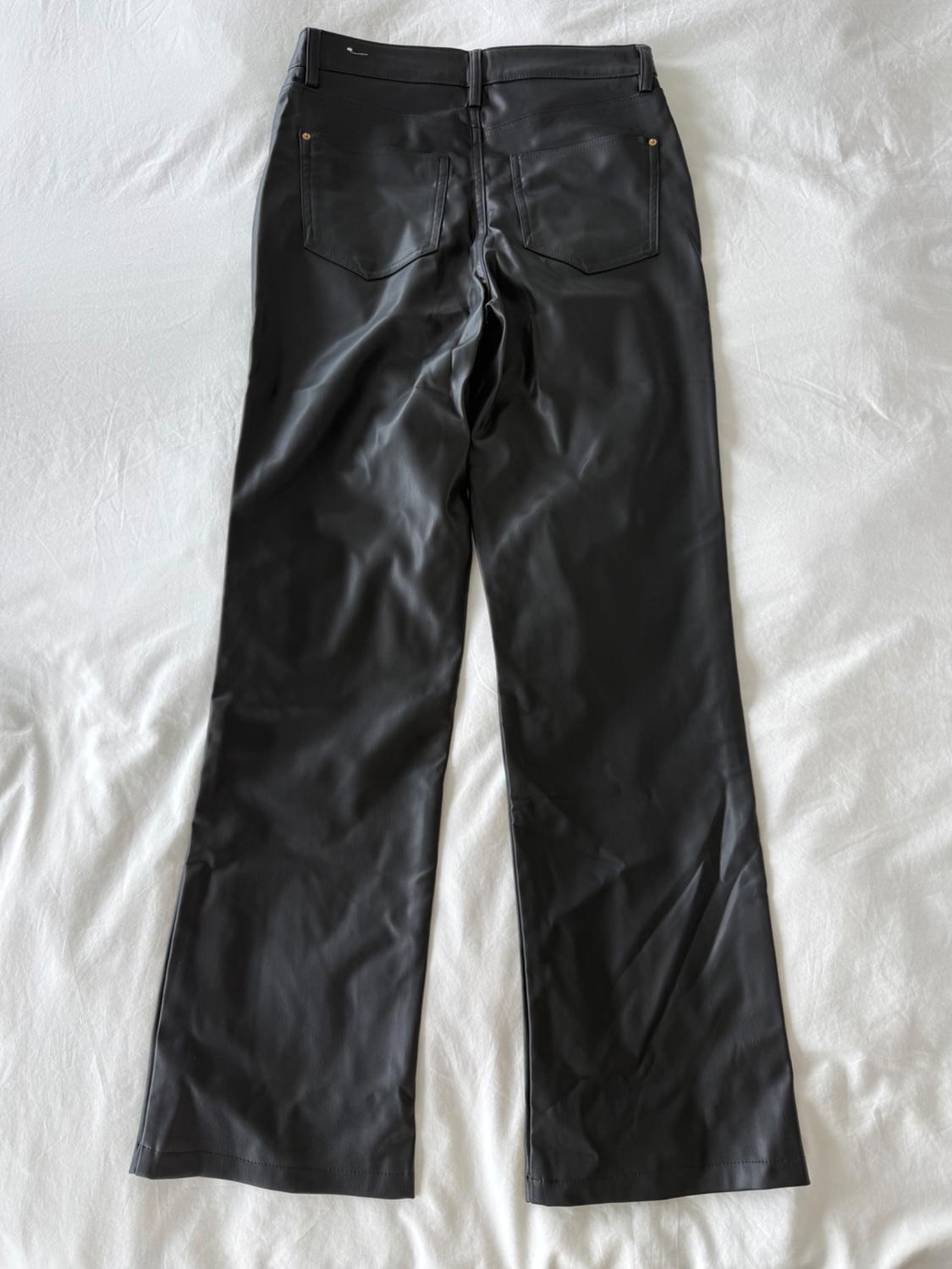 Black faux leather trousers with back pockets, placed on a white surface.