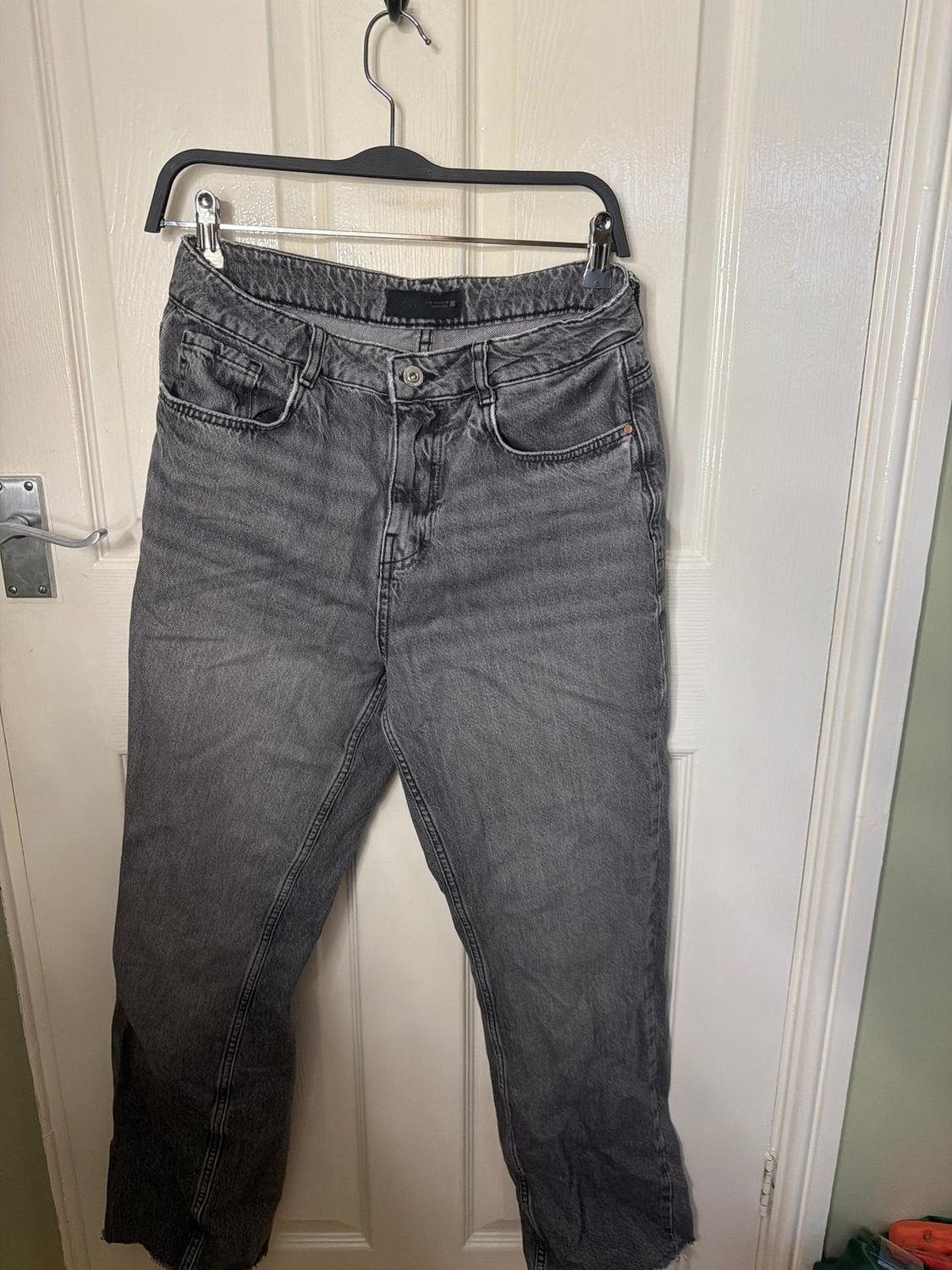 Grey jeans hanging on a black hanger over a white door.