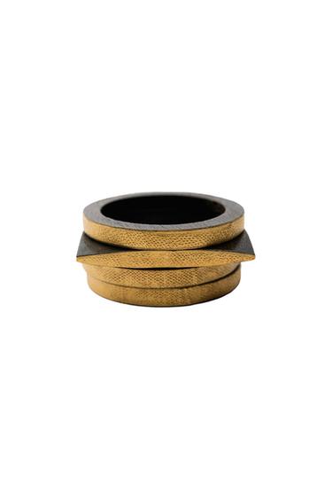 Three bracelets stacked on a white background. Two are round and the one in the middle is square, all with a gold-textured exterior and a dark interior.