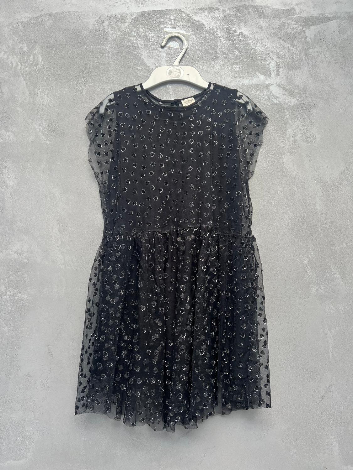 Black dress with a shimmering heart print, hanging on a white hanger against a textured grey background.