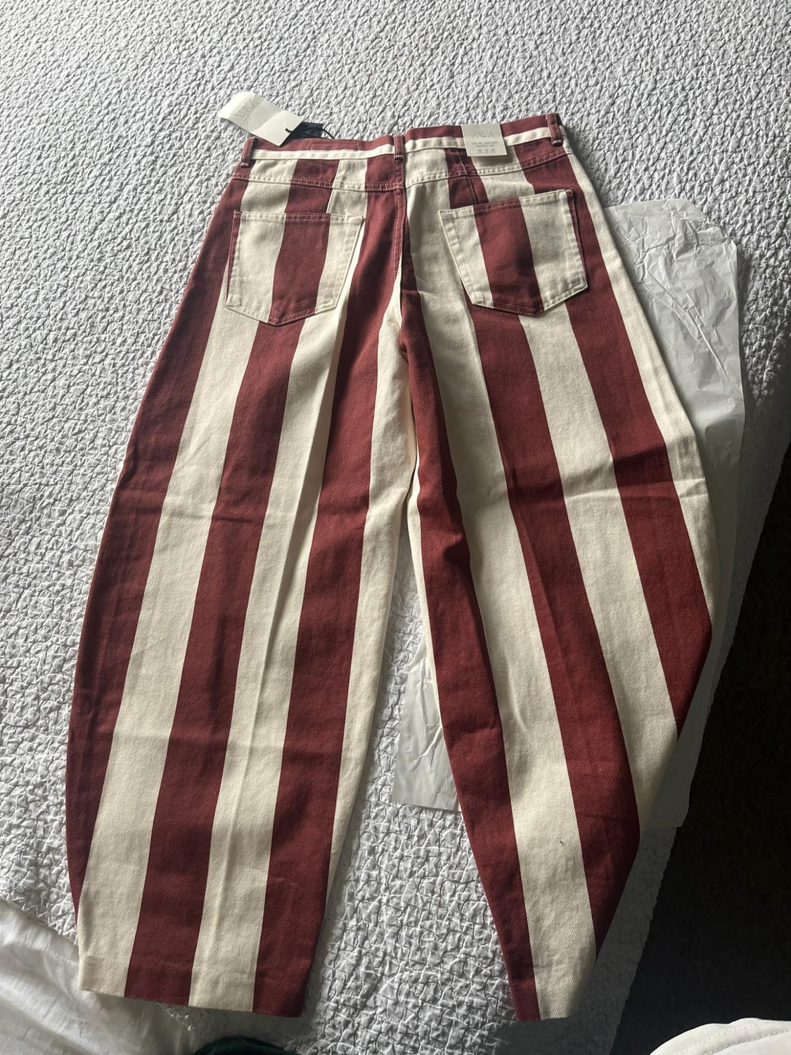 Maroon and cream vertical striped trousers viewed from behind on a white bedspread. They have a label with the text ZARA.
