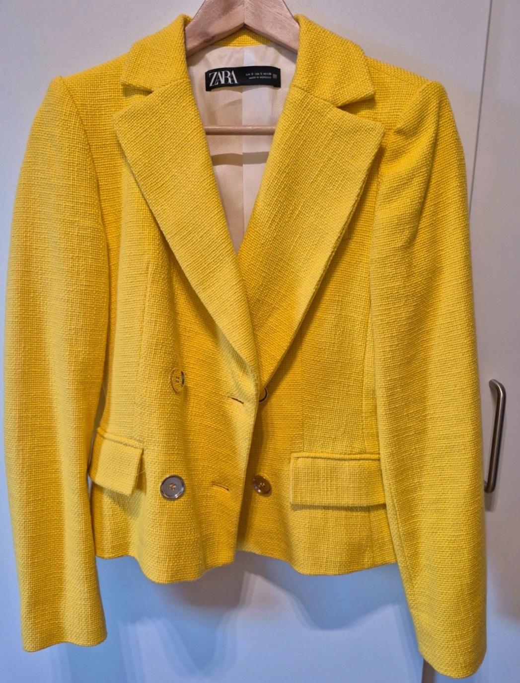 Textured yellow double-breasted blazer with pockets, hanging on a wooden hanger. Inner label with ZARA text.