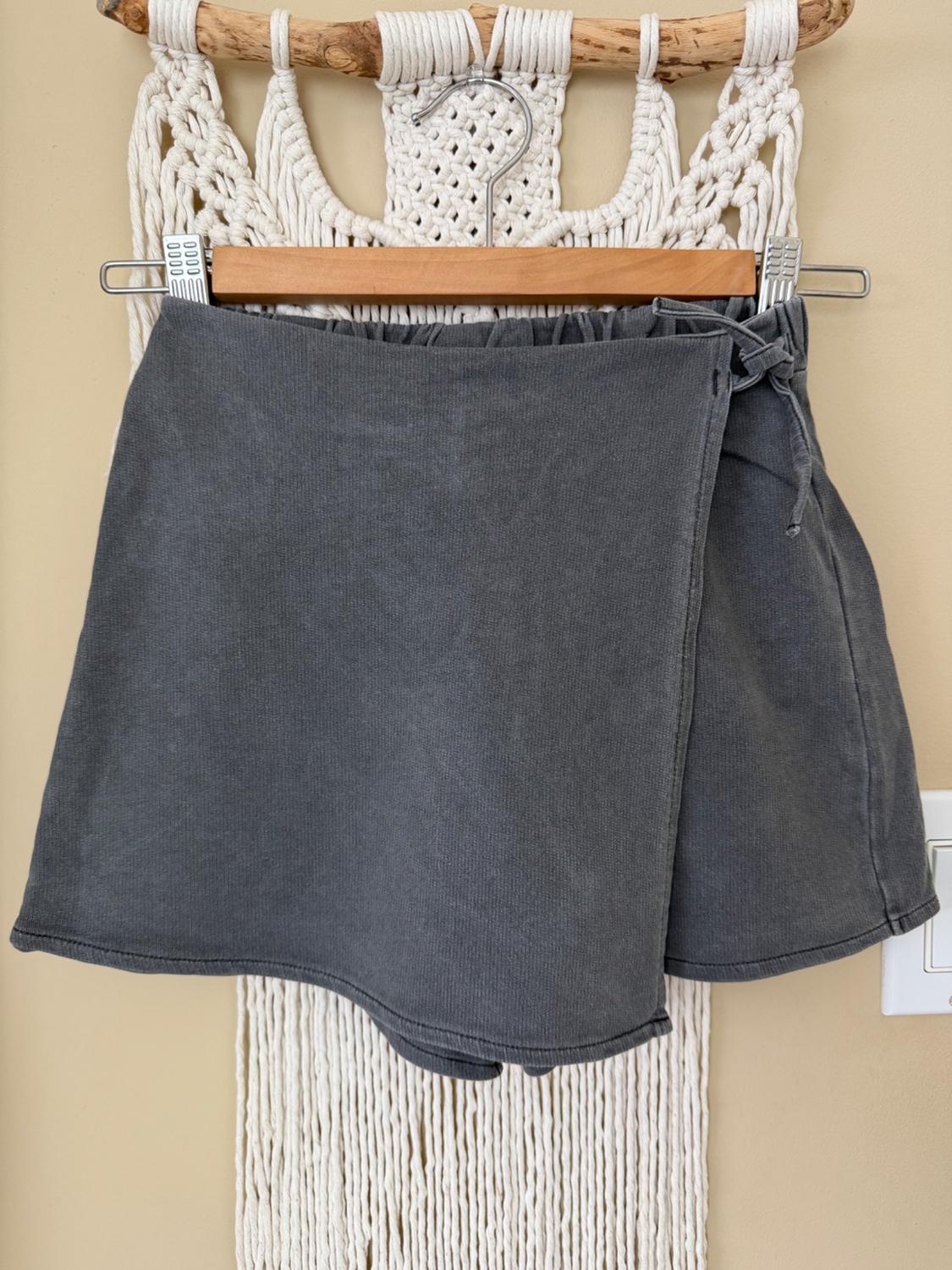 Gray skirt hanging on a wooden hanger against a white macrame background, with a visible switch on the right.