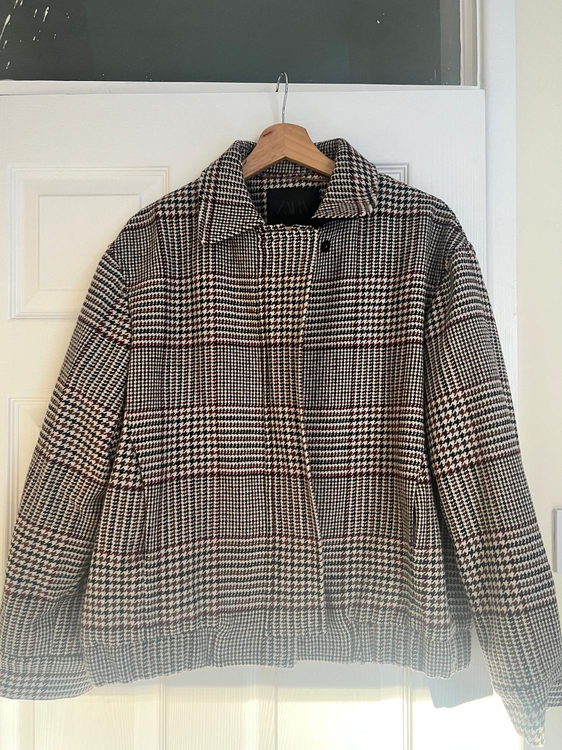 Brown and black checked jacket hanging on a wooden hanger over a white door.